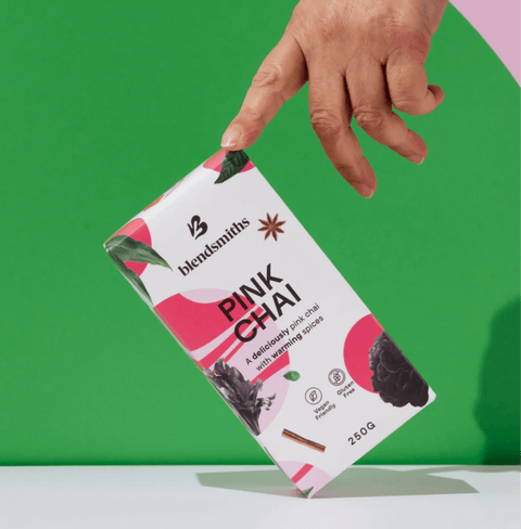 Hand holding a box of Pink Chai with beetroot and spices against a green background.