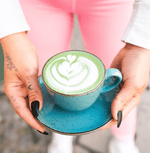 Person holding a blue cup of organic ceremonial matcha, showcasing latte art and Japanese tradition.