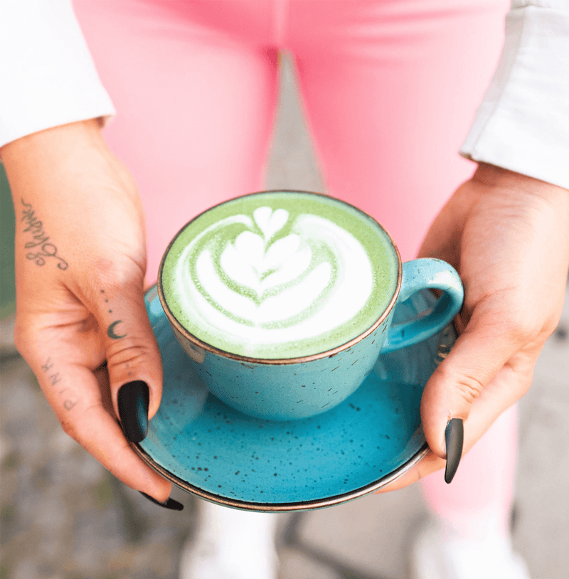 Person holding a blue cup of organic ceremonial matcha, showcasing latte art and Japanese tradition.