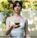 Golden Grade Matcha Uji usucha in a glass cup, held by a woman outdoors, vibrant deep green and smooth.