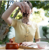 100 years old Wakōcha (Japanese Black Tea) loose leaves pouring from hand beside teapot and cup