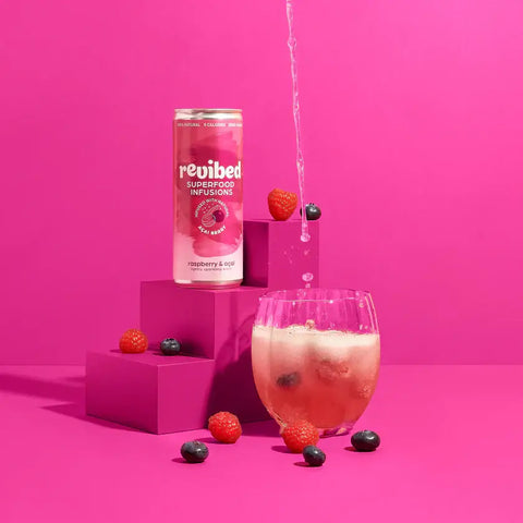 Revibed Raspberry & Acai Superfood Infusion with fresh berries, highlighting its fizzy, fruity blend on a vibrant pink backdrop.