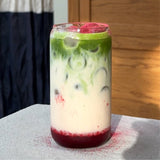 A pouch of Perfected Matcha Strawberry Matcha Powder with a whisk and a prepared matcha latte. — view 2