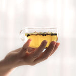 Clear glass cup of Cinnamon Orange Tea held in hand, showcasing golden color and fragrant spices.