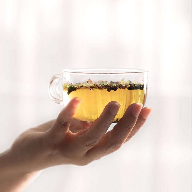Clear glass cup of Cinnamon Orange Tea held in hand, showcasing golden color and fragrant spices.