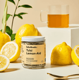 Tulsi Lemon-Aid tea blend jar with fresh lemons and brewed tea in a glass, perfect for a refreshing sip.