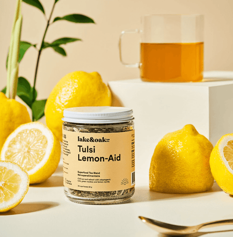 Tulsi Lemon-Aid tea blend jar with fresh lemons and brewed tea in a glass, perfect for a refreshing sip.