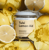 Tulsi Lemon-Aid tea blend jar surrounded by lemons and yellow flowers, a refreshing and healthy beverage choice.