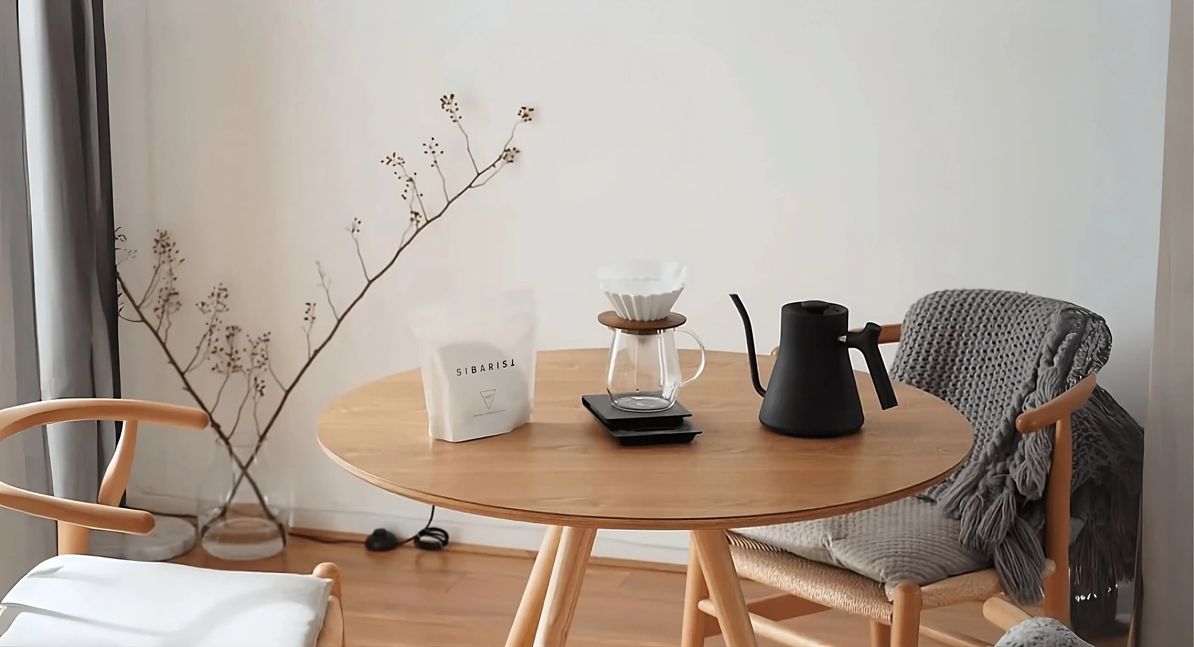 Round wooden table with coffee-making items in a room with chairs and decor.