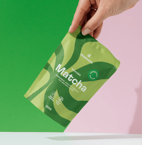 Hand holding a package of Wakaba Ceremonial Matcha against a green and pink background.